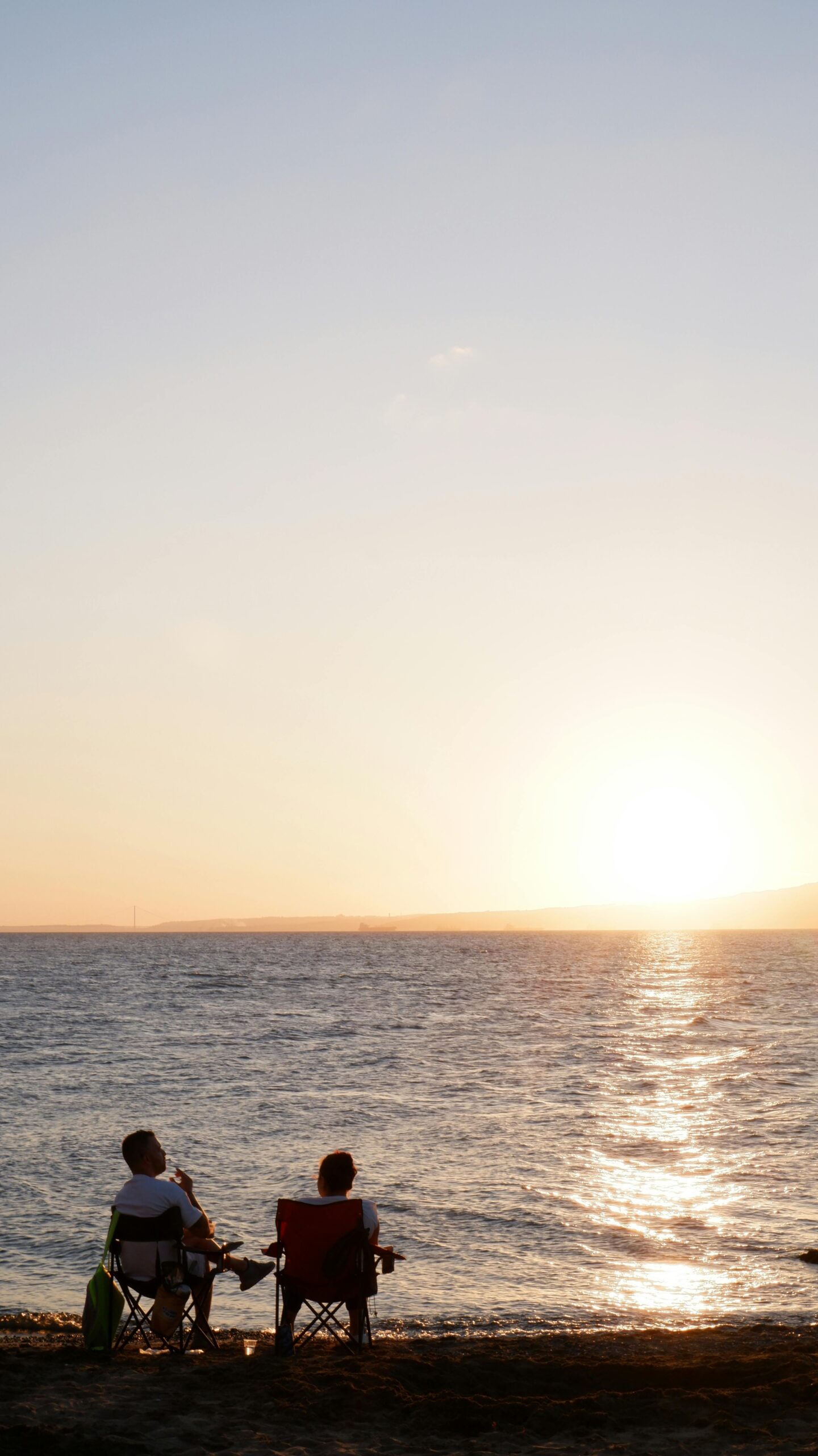 A couple enjoying a peaceful seaside sunset seated on beach chairs, creating a tranquil atmosphere.