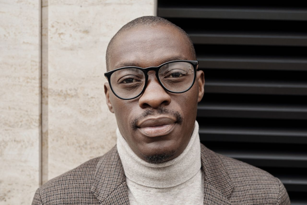 Close-up portrait of a man in eyeglasses and turtleneck, exuding confidence.